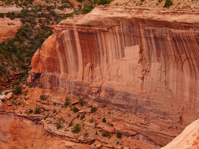 [A wall of rock with vertical bands of color ranging from light pink to dark brown. Amid this are parts of the wall worn away and look almost like a grouping of people.]